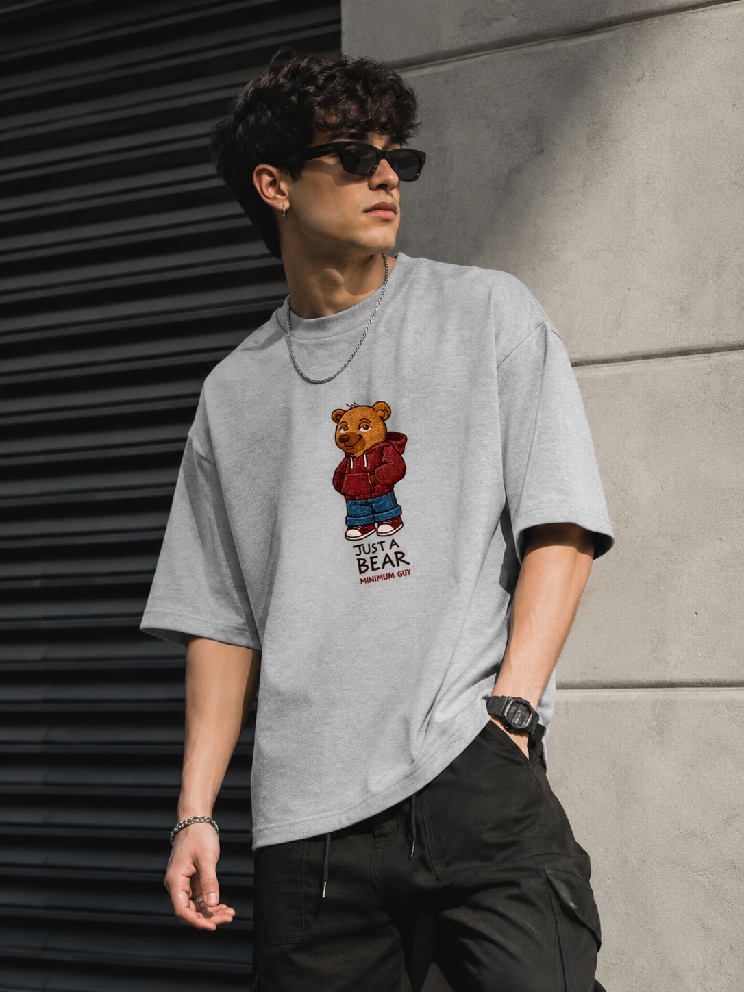 Man wearing a gray t-shirt with a bear graphic design, standing against a concrete wall.