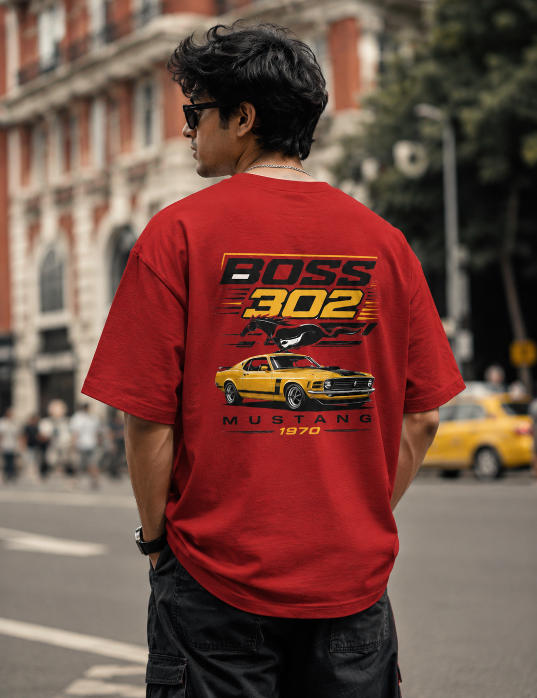 Person wearing a red t-shirt with a car graphic and text on the back, standing on a street.